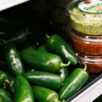 Fresh jalapeño peppers next to tubs of guacamole and salsa on a supermarket refrigerated shelf